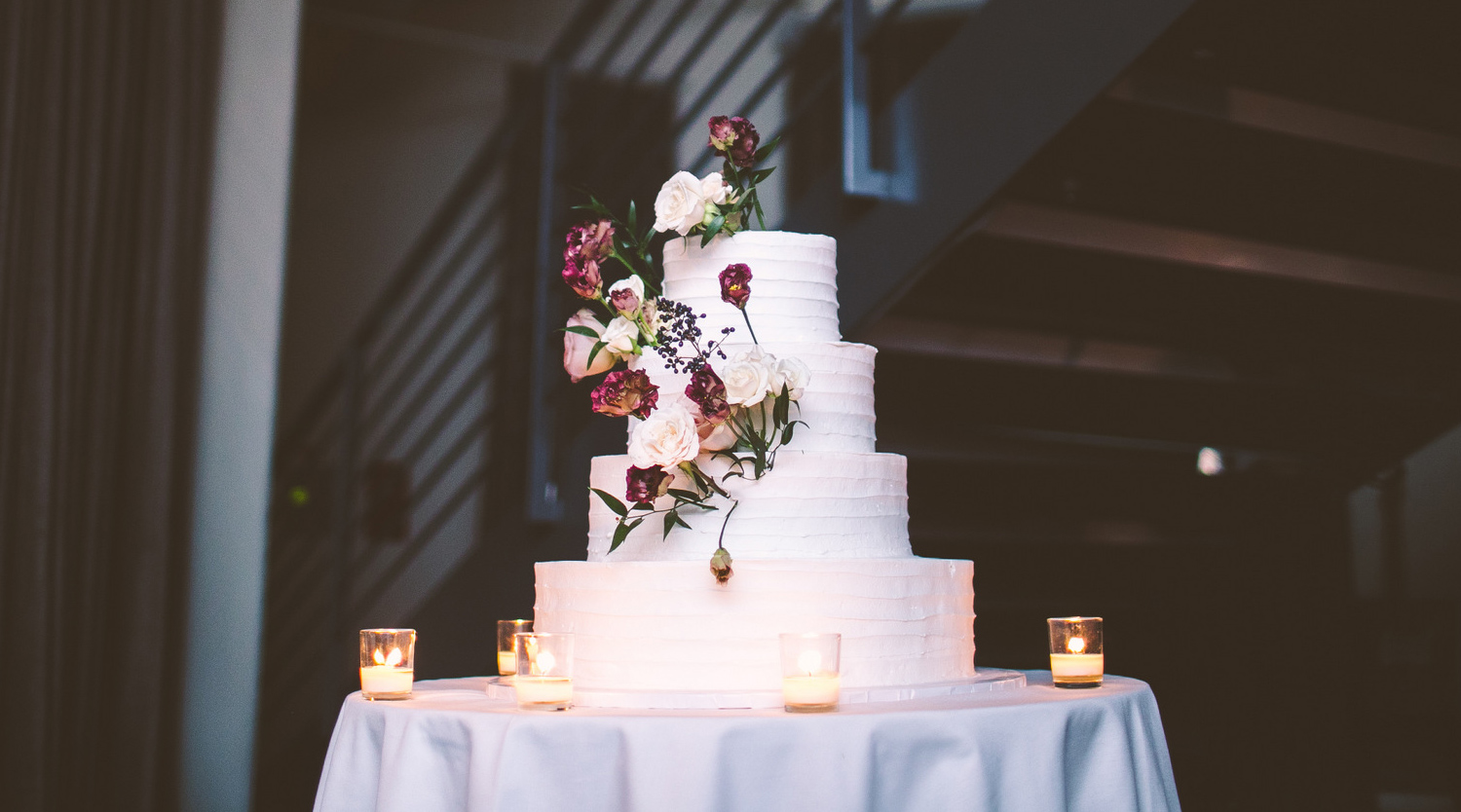 Photo: white frosted wedding cake, flowers and leaves sticking out of the four tiers